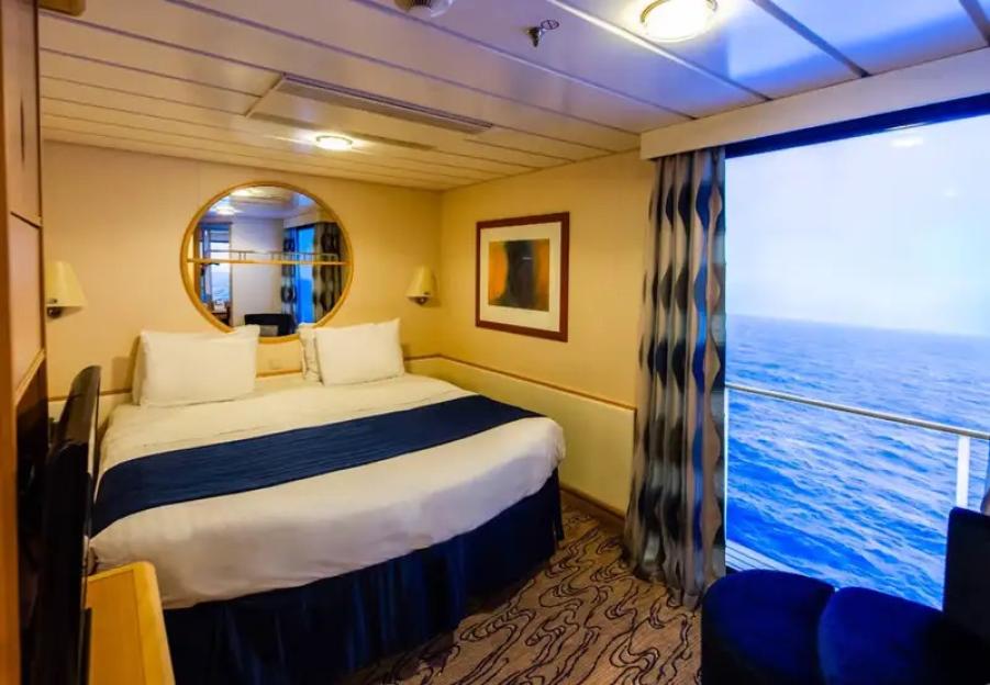 Cruise ship cabin with a bed, a circular mirror, and an ocean view through a large window.
