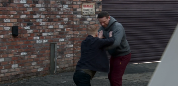 Two men grappling in a brick alleyway.