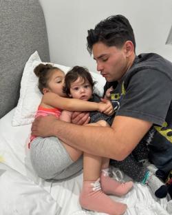 Man hugging two young children on a bed.