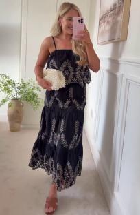 Woman in a black embroidered maxi dress and sandals holding a pearl clutch.