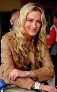 Woman with long blonde hair wearing a tan leather jacket.
