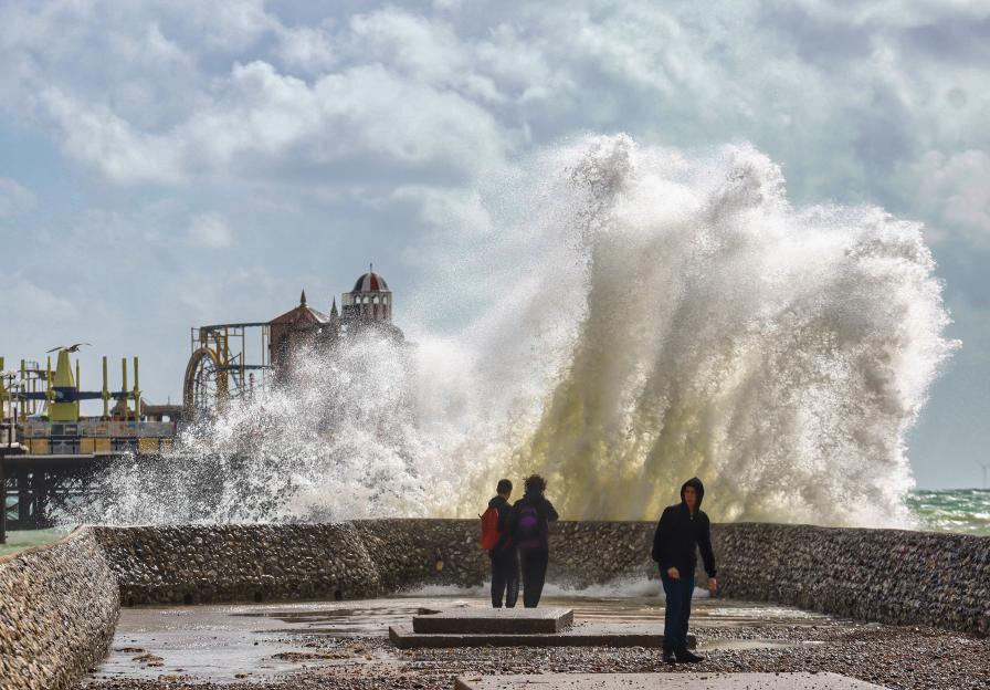 Large waves crashing against a seawall with people watching.