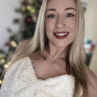 Woman in a sequined top in front of a blurred Christmas tree.