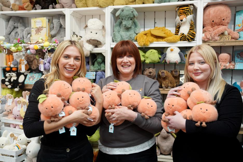 Three women holding peach plush toys in a shop.