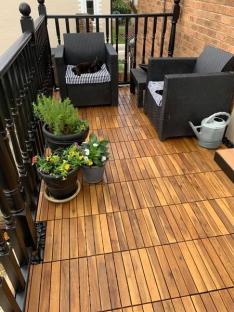 Wooden patio tiles on a balcony with black chairs and potted plants.