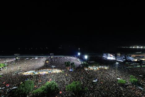 Lady Gaga performing at a large outdoor concert on Copacabana Beach at night.
