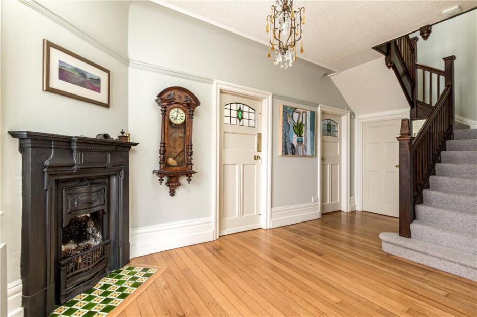 An empty hallway featuring a fireplace, wall clock, three doors, a chandelier, and a carpeted staircase.