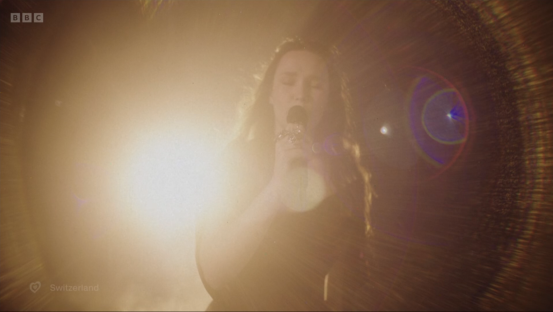 Screenshot of a woman singing into a microphone on stage.