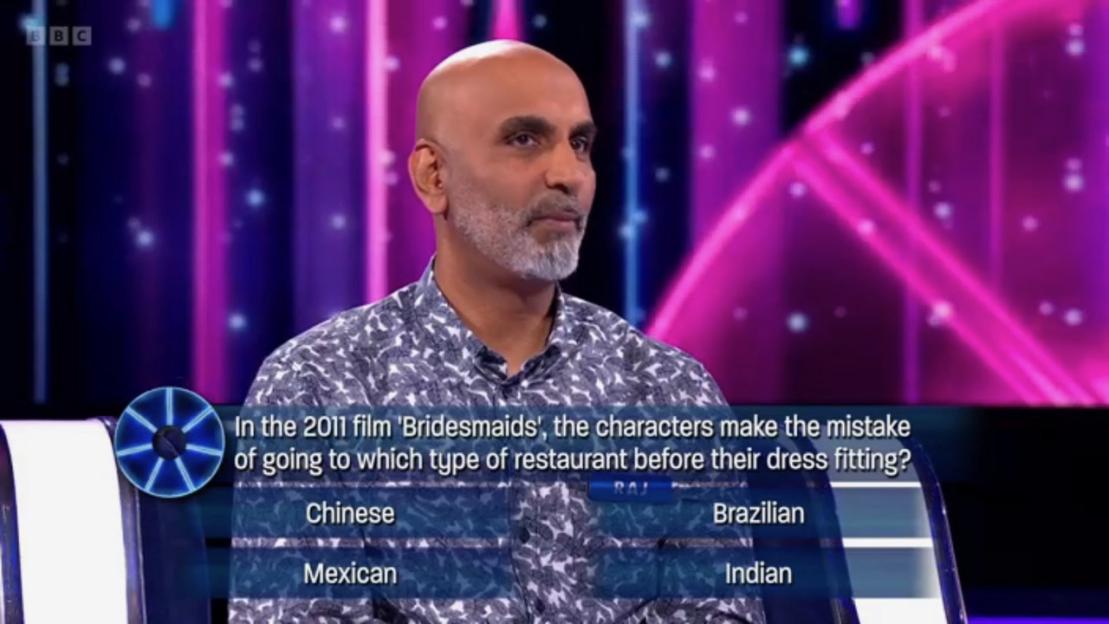 A man looks at a multiple-choice question on a TV game show: "In the 2011 film 'Bridesmaids', the characters make the mistake of going to which type of restaurant before their dress fitting?" The options are Chinese, Brazilian, Mexican, and Indian.