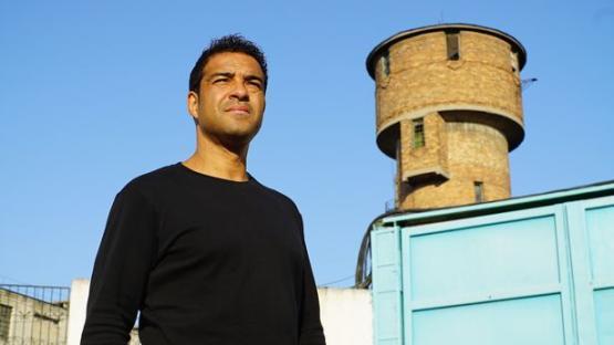 A man stands outside a prison, looking off to the side.