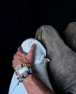 Person's hand resting on another person's lap, wearing several bracelets.