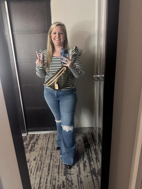 Woman in striped shirt and jeans making peace sign in mirror selfie.