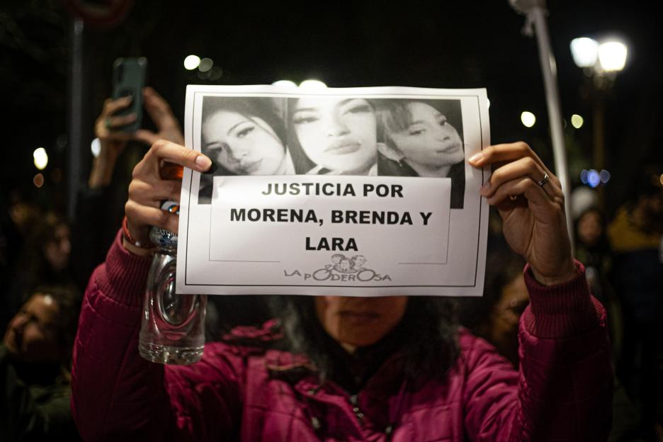 A person holds a sign with photos of Morena Verri, Brenda Loreley Del Castillo, and Lara Morena Gutiérrez, with the text "JUSTICIA POR MORENA, BRENDA Y LARA" (Justice for Morena, Brenda and Lara).