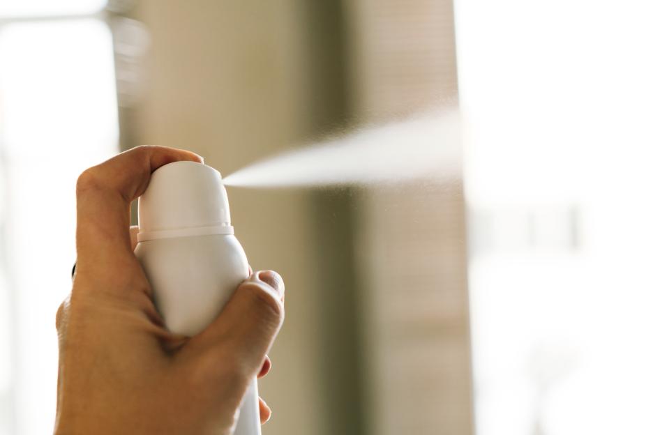 Hand spraying a white deodorant bottle.