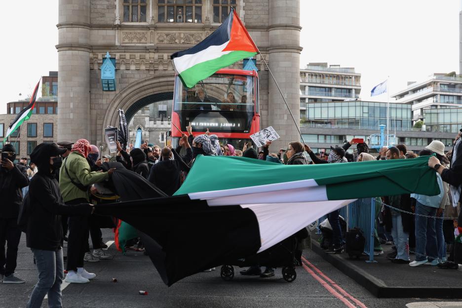 Pro-Palestine protesters blocking Tower Bridge in London with flags and signs.