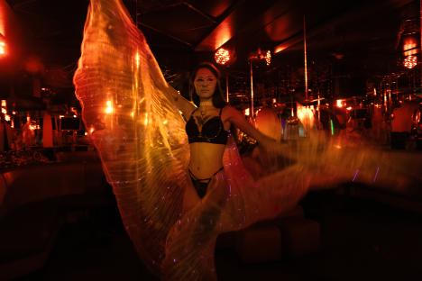 A dancer in a dimly lit nightclub in Kharkiv, Ukraine, wearing a mask and lingerie, poses with a glowing fabric.