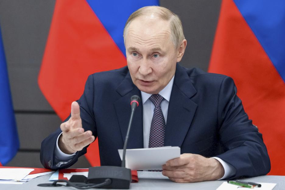Russian President Vladimir Putin speaks at a meeting, gesturing with one hand and holding papers in the other.