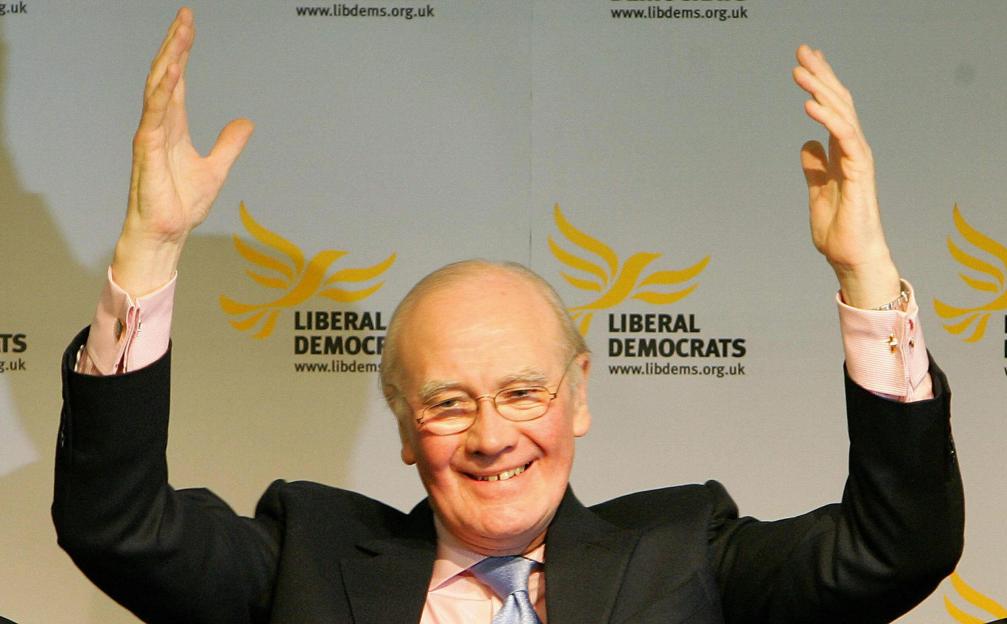 Sir Menzies Campbell, leader of the Liberal Democrats, raising his hands in front of party logos.
