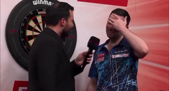 A darts player covers his face while being interviewed.