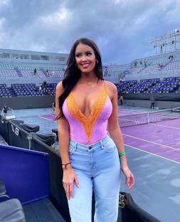 Woman in lavender and orange lace bodysuit and light blue jeans at a tennis stadium.