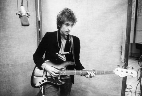 Black and white photo of Bob Dylan playing a Fender Jazz bass guitar in a recording studio.