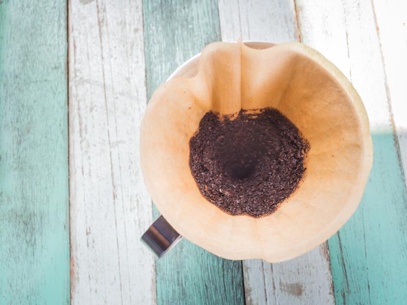 Top view of a used coffee filter with ground coffee beans on a wooden table.