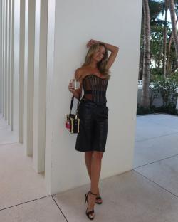 Woman in black corset and leather shorts holding a drink.