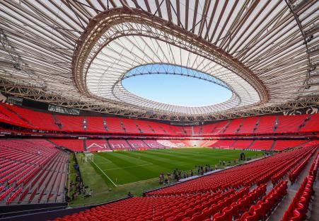 Empty stadium with red seats and a green field.