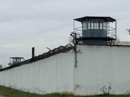 Exterior of a prison with a high wall, barbed wire, and guard towers.