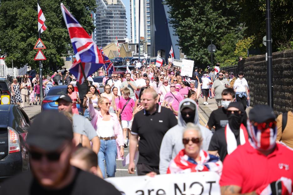 A large group of protesters marching down a street, many wearing pink and carrying Union Jack flags.