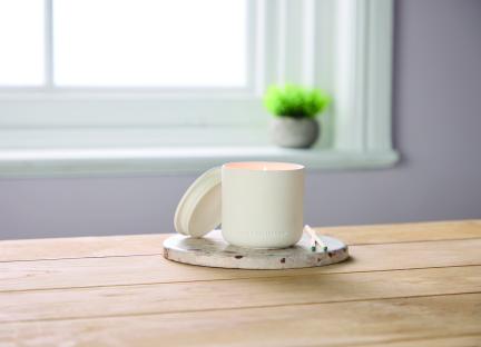 A lit white candle with its lid on a coaster.