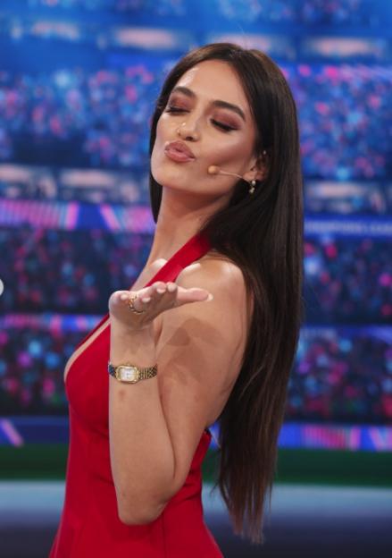 Woman in a red dress with a microphone on her cheek, blowing a kiss to the camera.
