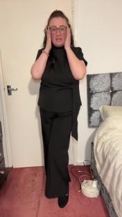 Woman in black pantsuit expressing surprise.