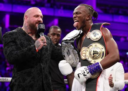 KSI celebrates a boxing victory, holding championship belts.