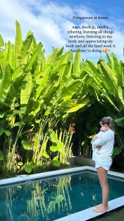 Woman holding newborn baby by a pool, surrounded by lush tropical plants.