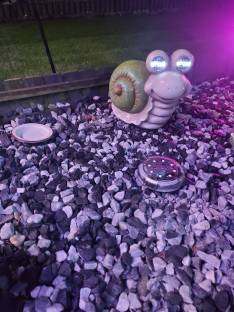 Light-up snail garden statue on gravel.