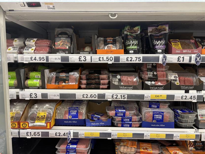 Refrigerated shelf of various meat products in a grocery store, with prices displayed.