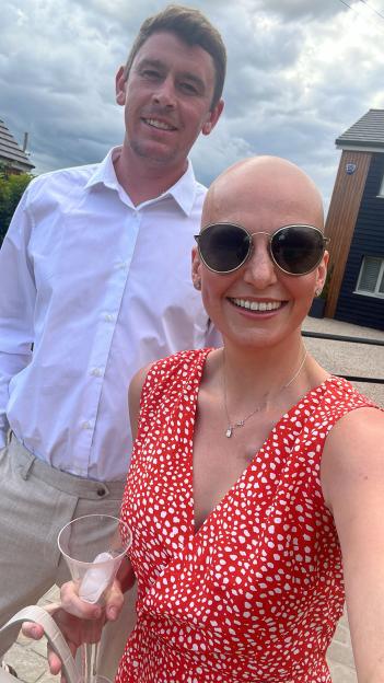 Woman with shaved head and sunglasses stands with a man.