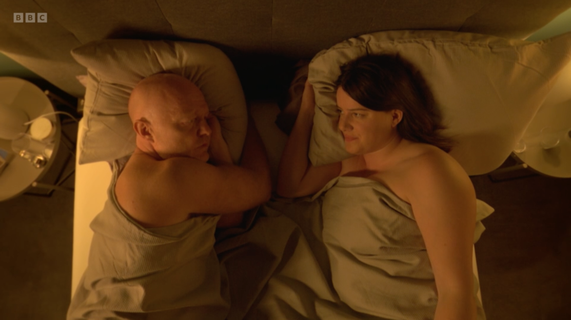 Screenshot of a man and woman lying in bed.