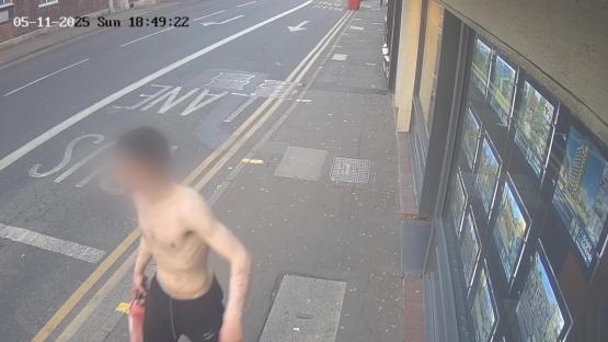 Surveillance image of a shirtless man carrying a fire extinguisher.