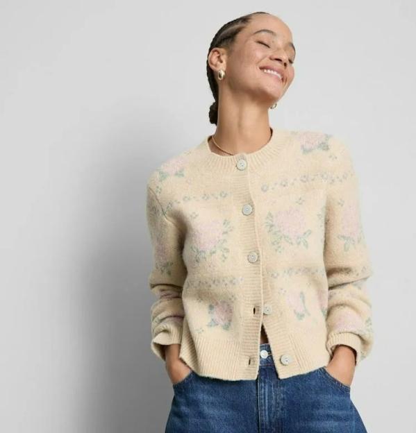 Woman wearing a cream cardigan with pink and green floral embroidery and blue wide-leg jeans.