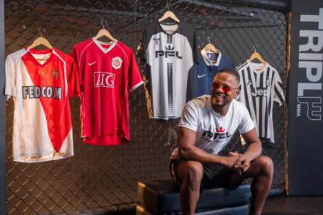Man in sunglasses sits smiling in front of several jerseys.
