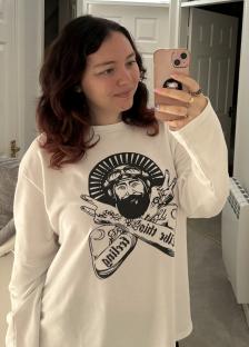 Woman taking a selfie wearing a white sweatshirt with a graphic design.