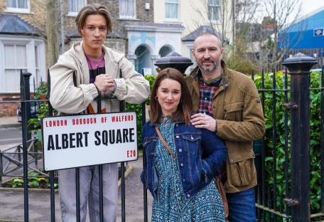 Photo of three actors from EastEnders standing by an Albert Square sign.