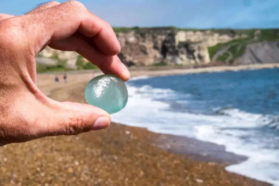 Hand holding a piece of sea glass on a beach.