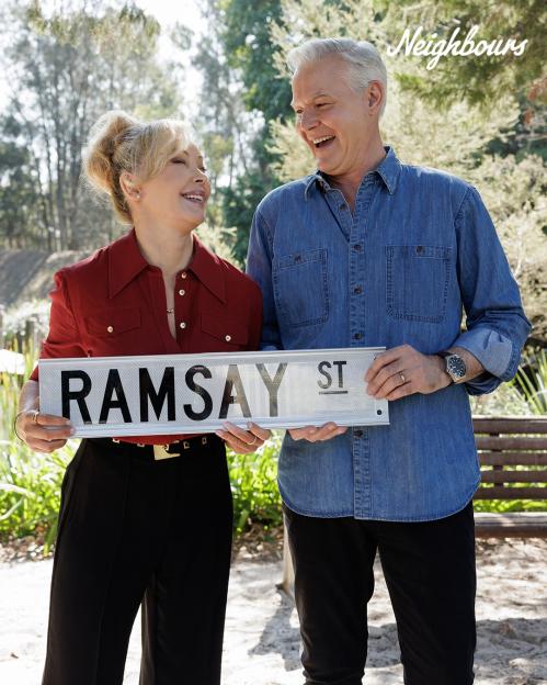 Two smiling actors holding a Ramsay St. sign.