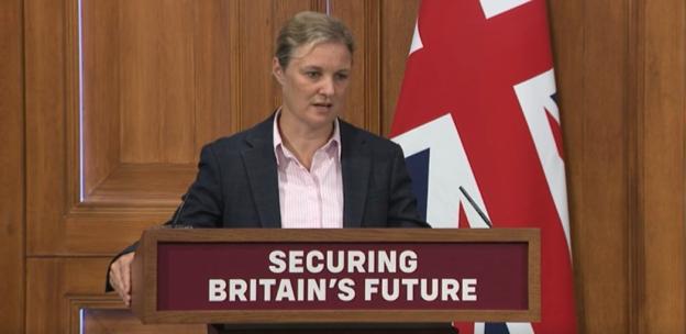 Screenshot of a news broadcast showing a woman speaking at a podium with