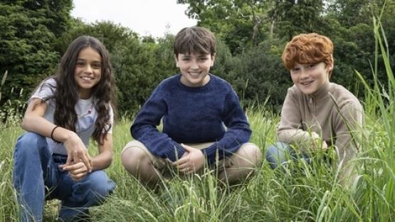 Three children crouching in tall grass.
