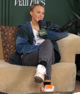 Woman sitting on a couch, speaking into a microphone.