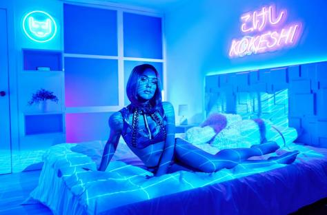 Illustration of a female robot sitting on a bed in a futuristic city.